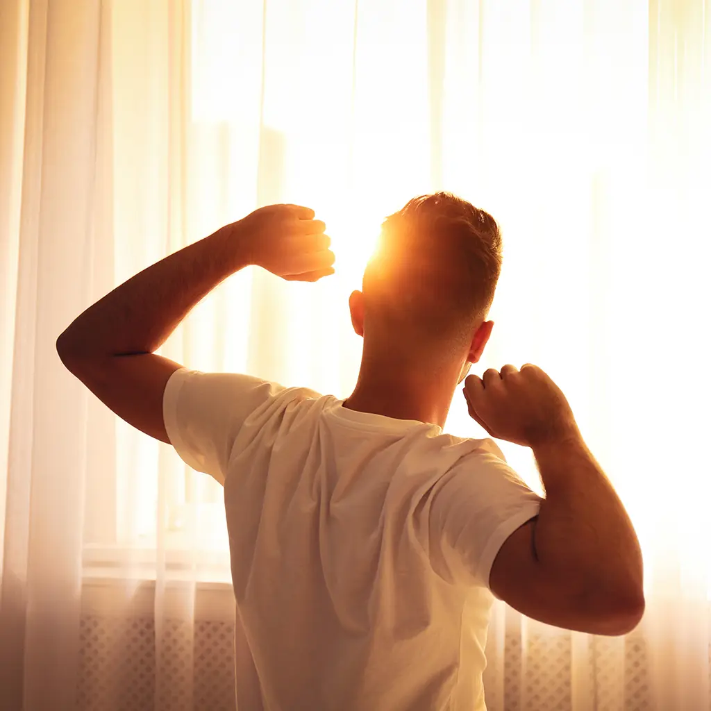 Mann nach dem Aufstehen sieht Richtung Sonnenaufgang