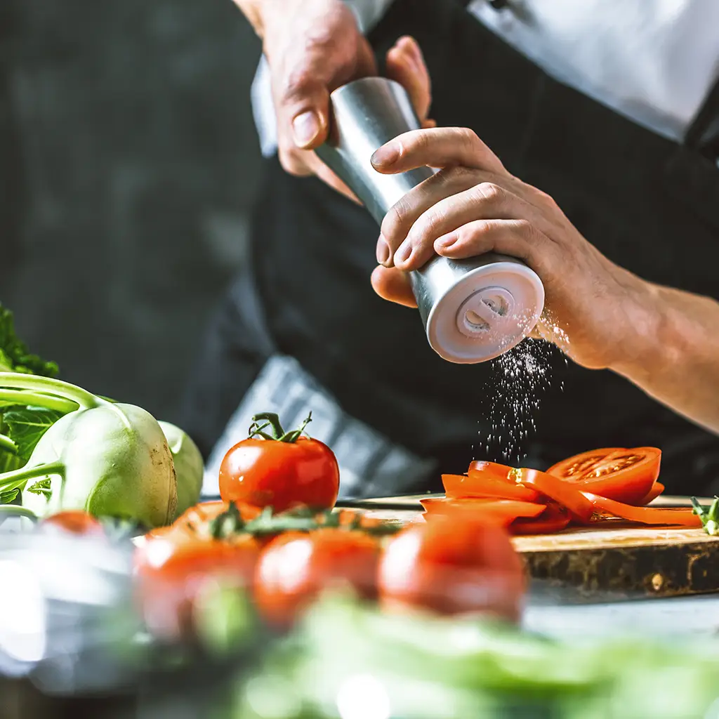 Mann in Küche salzt geschnittene Tomaten